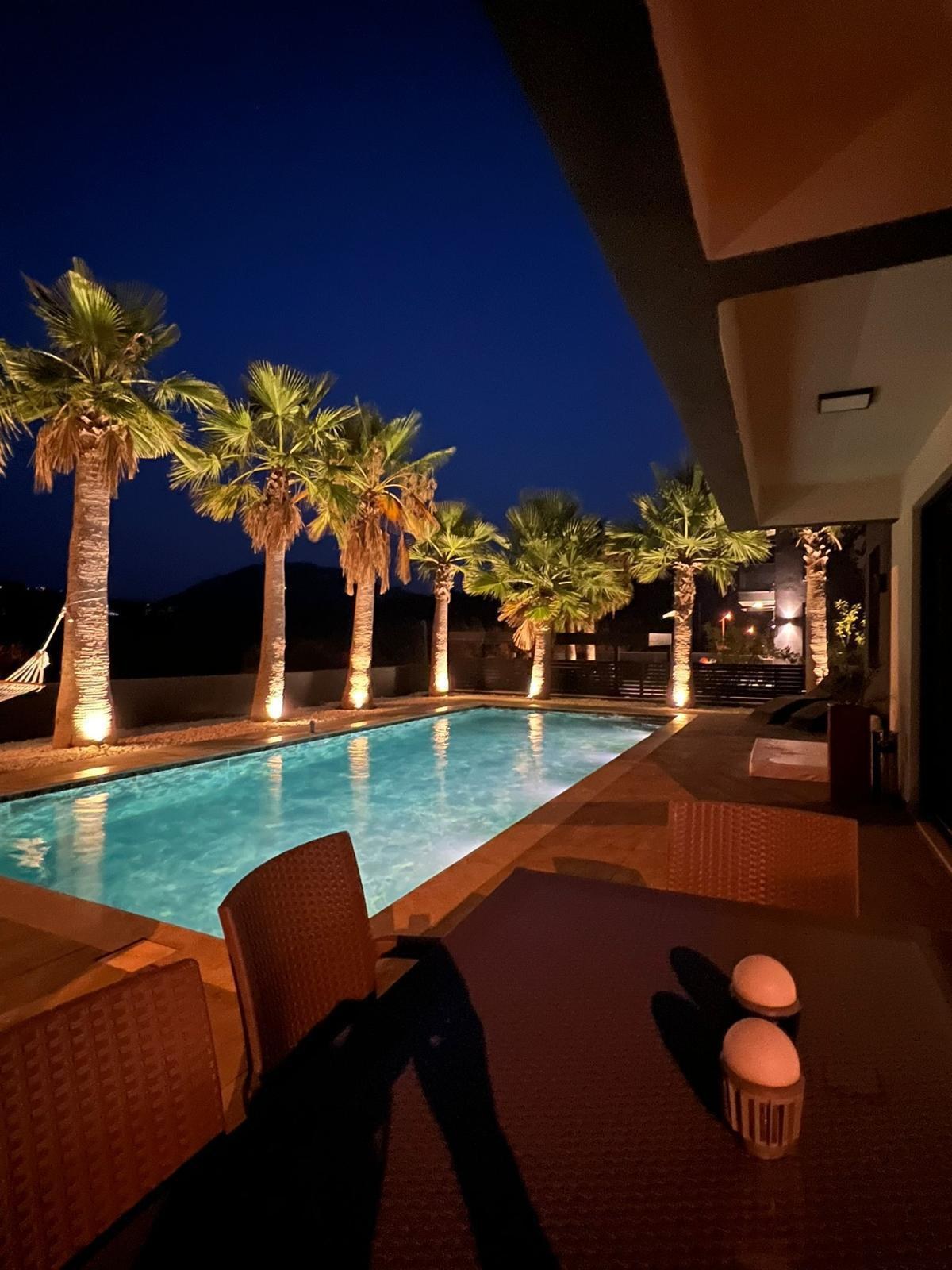 The Pool House Time villa and private pool lit at night, framed by palm trees